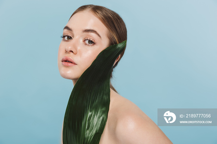 Beautiful young woman take care of her skin isolated over blue wall background posing with leaf flow