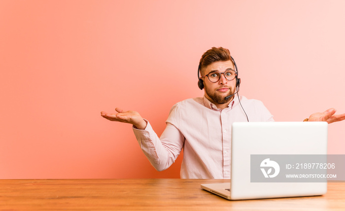 Young man working in a call center doubting and shrugging him shoulders in questioning gesture.