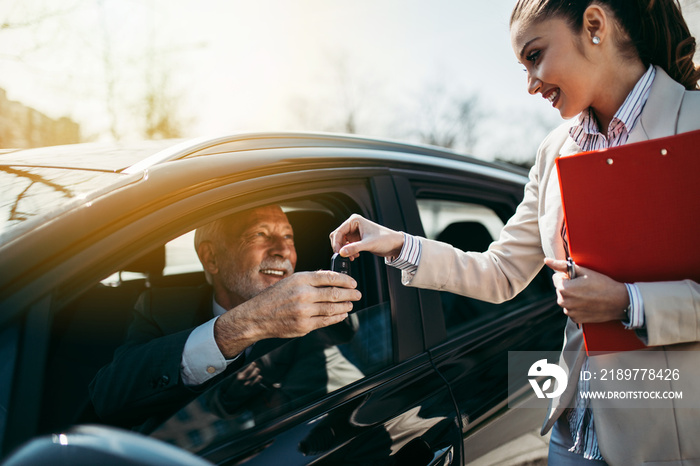 Young woman car dealer gives the keys to the new owner. Hands with keys close up.