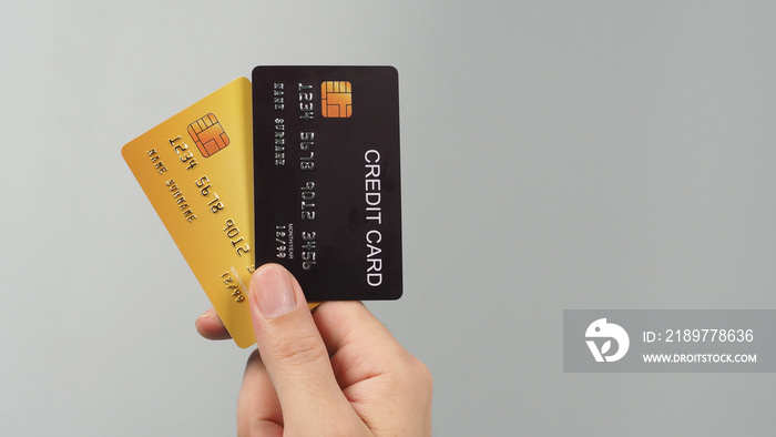 Hand is hold two credit cards. Black and gold color credit cards isolated on grey background.