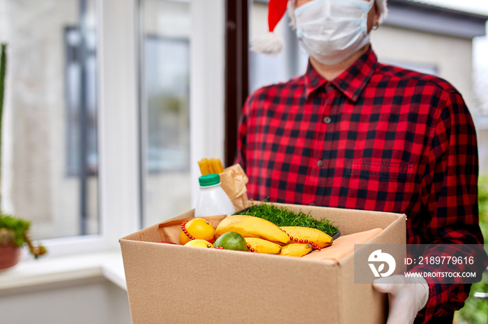 Volunteer man in Santa hat and protective mask and gloves delivery donation box at home in Christmas