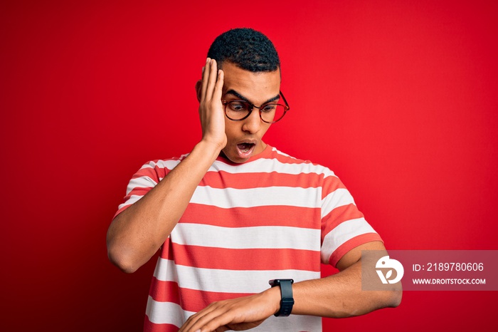 Young handsome african american man wearing casual striped t-shirt and glasses Looking at the watch 