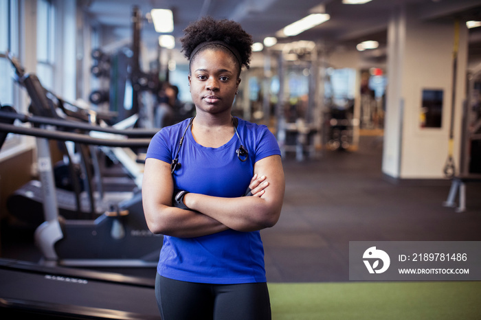 Portrait of confident serious female athlete with arms crossed standing in gym