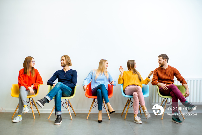 Portrait of a young people dressed casually sitting in a row on the colorful chairs on the white wal