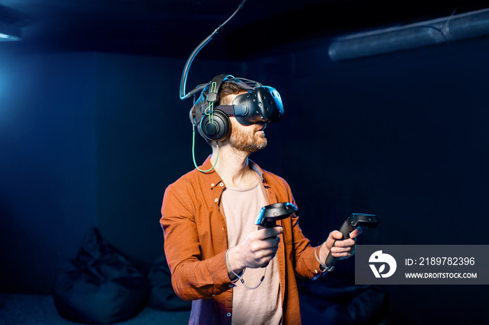 Man playing game using virtual reality headset and gamepads in the dark room of the playing club