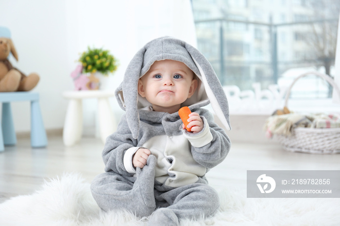 Cute little baby in bunny costume sitting on furry rug and eating carrot
