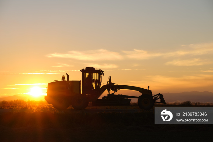 Silhouette of heavy duty tractor driving on road at sunset