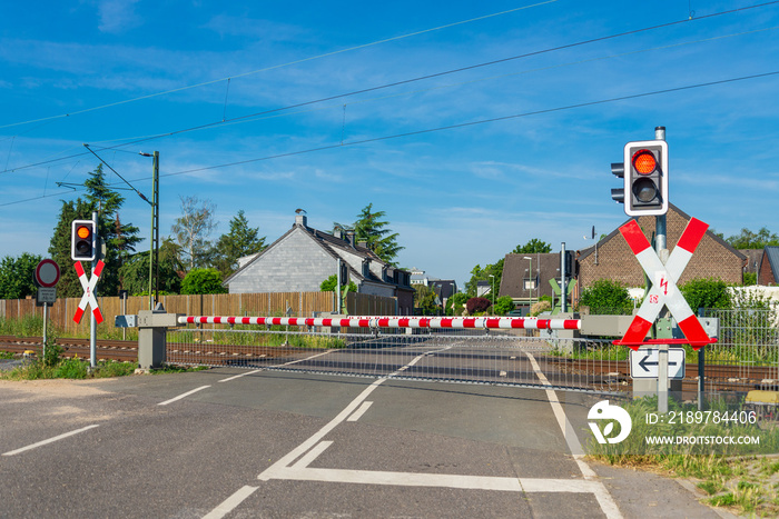 Outdoor sunny street view of level crossing railway barrier and red traffic light at intersection be