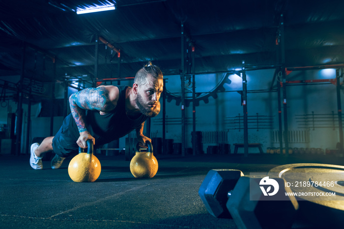 Young healthy man athlete doing push-ups with the weights in the gym. Single male model training and