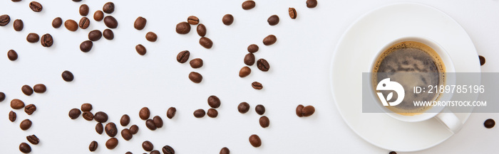top view of delicious coffee in cup near scattered roasted beans on white background, panoramic shot