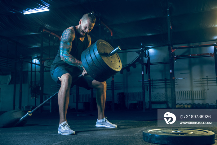 Young healthy man athlete doing exercise with the barbell in the gym. Single male model training har