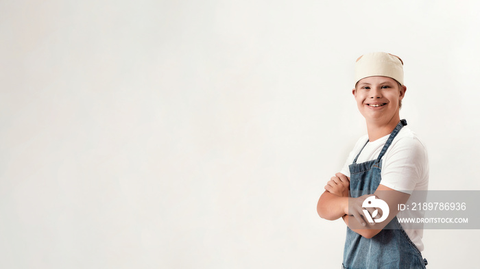 Disabled boy with Down syndrome dressed as a cook in apron and hat smiling at camera while standing 