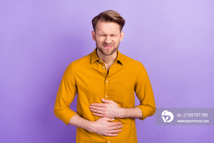 Photo of displeased young man closed eyes hands on stomach feel bad isolated on violet color backgro