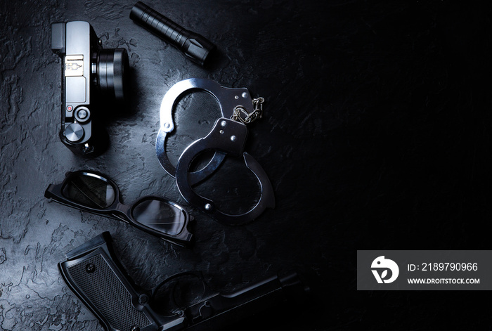 黑色背景上有黑色的枪、手电筒、眼镜、相机和警用金属手铐。