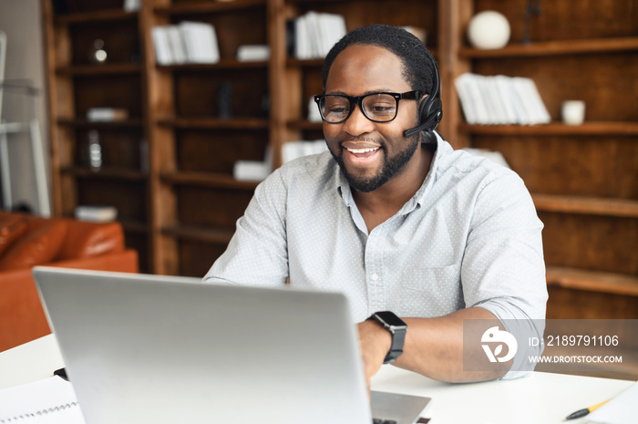 A multiracial guy using a hands free device for online communication sitting at the desk in modern o