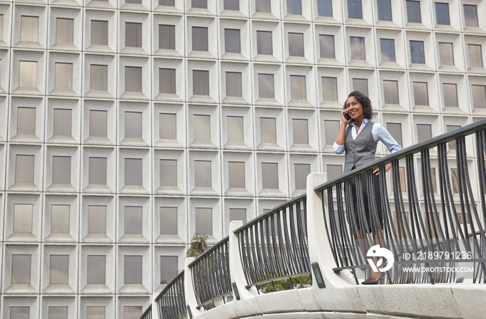 Business woman standing behind railings in front of built structure, using smartphone to make call