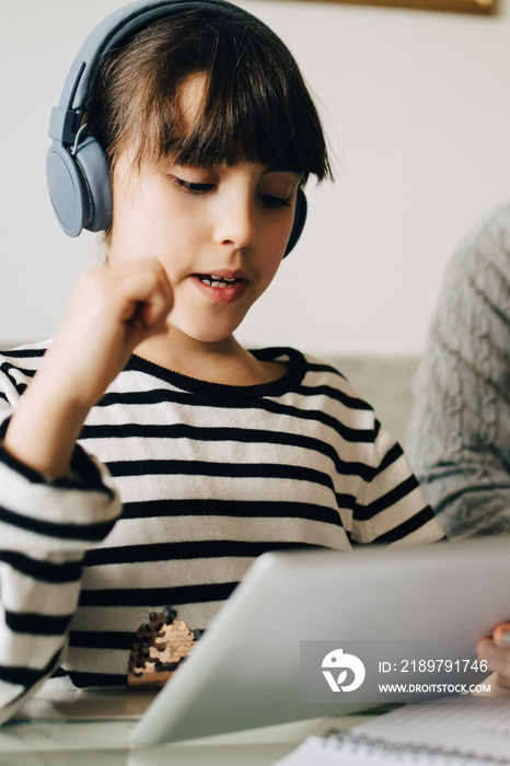 Girl wearing headphones while using digital tablet while studying at home