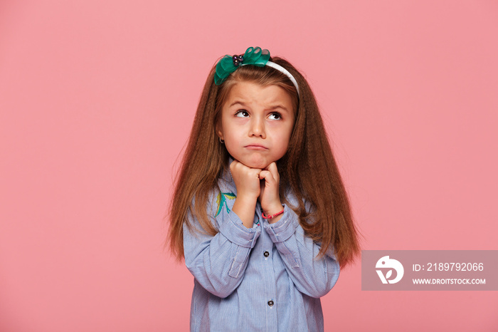 Close up photo of adorable schoolgirl 5-6 years propping up her head with fists being upset or dream