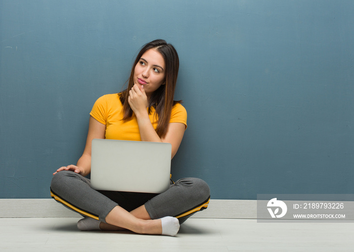 Young woman sitting on the floor with a laptop doubting and confused