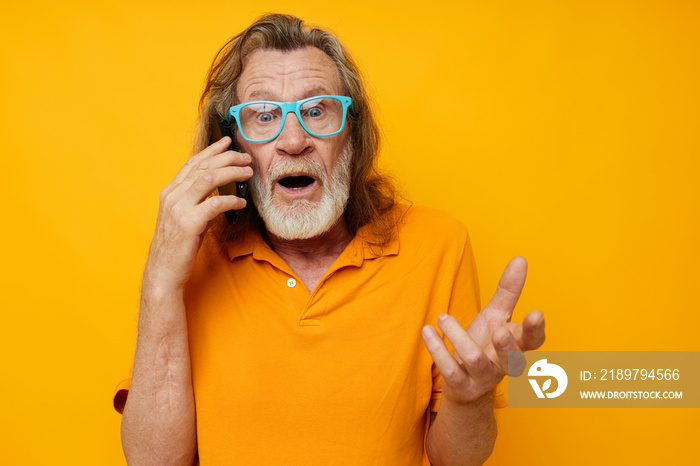 Portrait of happy senior man wearing blue glasses yellow shirt talking on the phone yellow backgroun