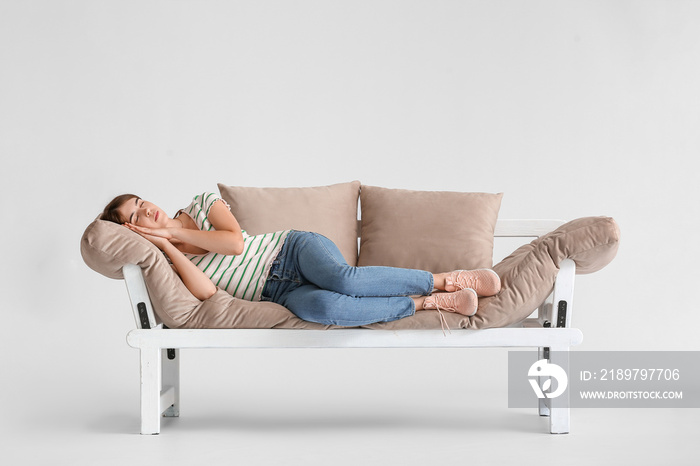 Young woman sleeping on modern sofa against light background