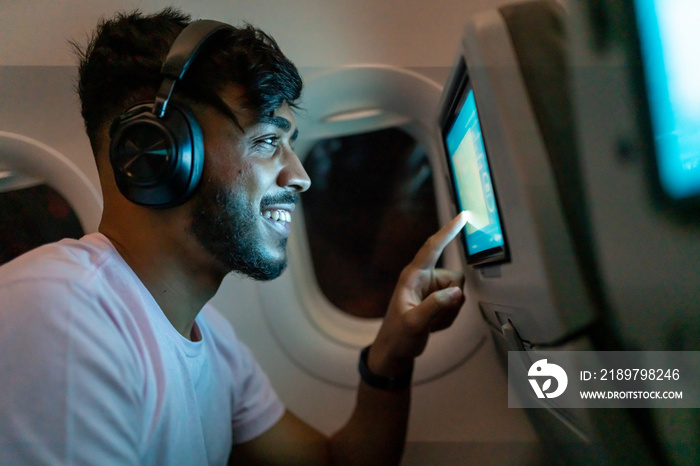 Passenger in airplane touching LCD entertainment screen. Latin american man in plane cabin using sma