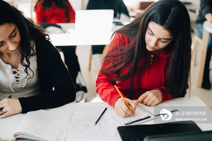 High angle view of female students writing in book while learning at classroom