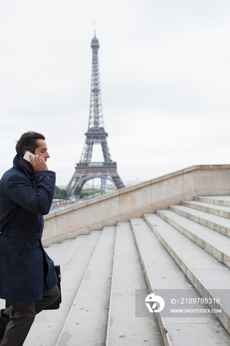 Businessman talking on smart phone on steps, Eiffel Tower, Paris