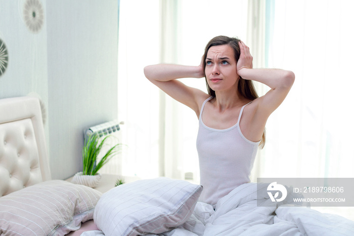 Young woman suffering and disturbed by noisy neighbors and covering her ears with hands while trying