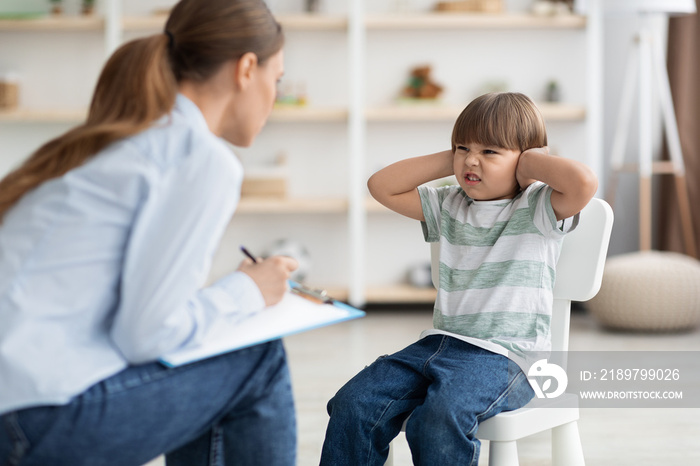 Professional psychotherapist trying to talk to difficult kid, grumpy little boy covering ears and fr