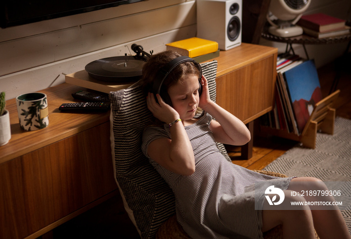 High angle view of girl with eyes closed listening music while sitting on chair at home