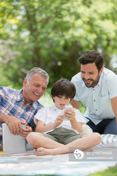 Multi-generation family, using smart phone on picnic blanket in park