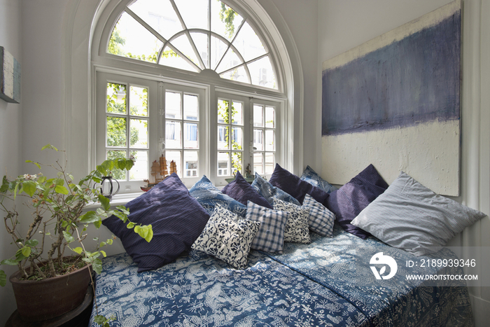 Comfy bed with house plant against arched French window at home