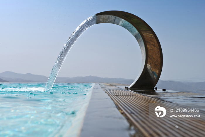 A curved stainless steel water fountain with water flowing 