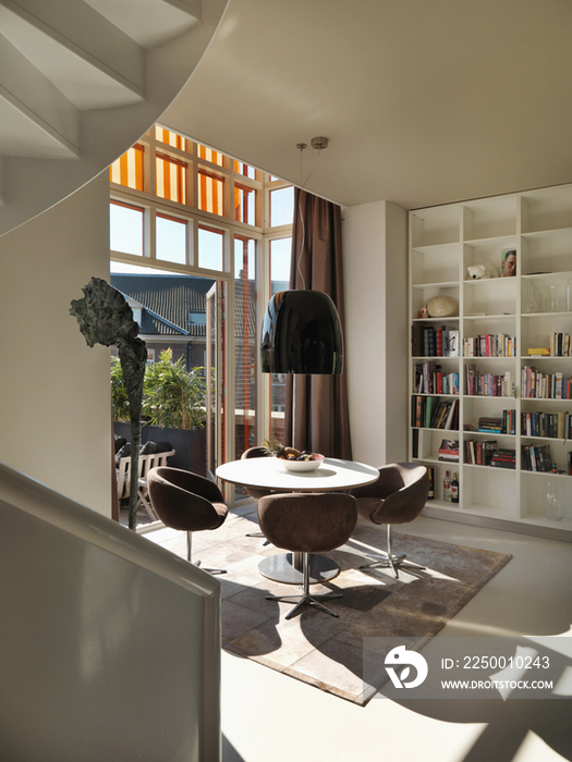 Four elegant chairs and round table by book shelf and window at contemporary house