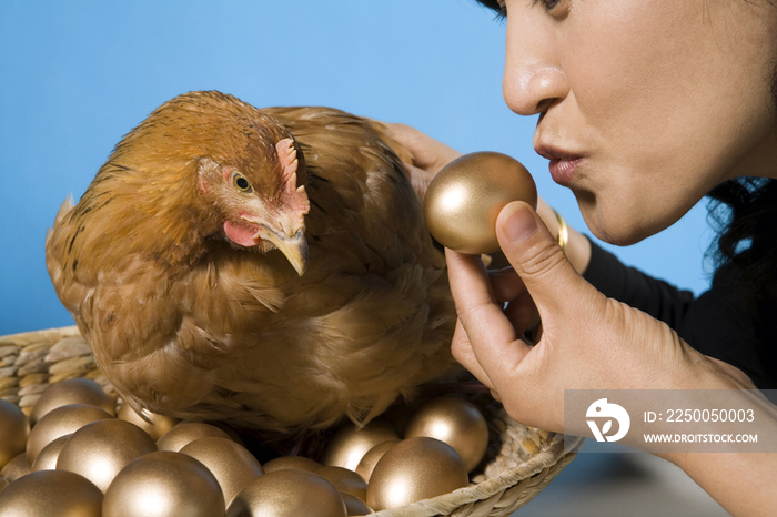 一位中年女性手拿一个金蛋，正抚摸着一只孵金蛋的鸡
