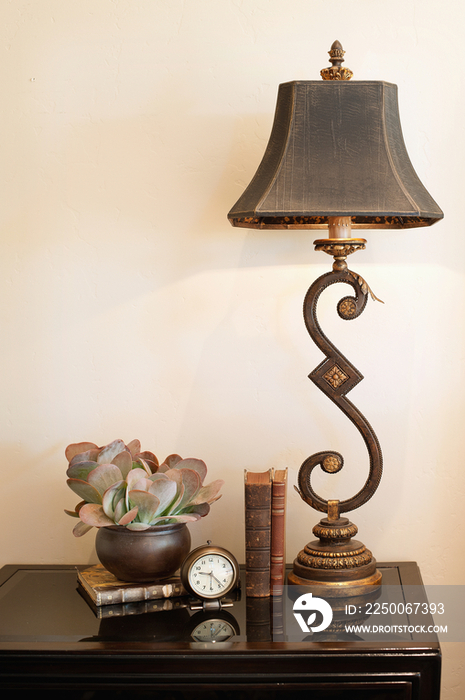 Lamp with books; clock and vase on console table against wall at home