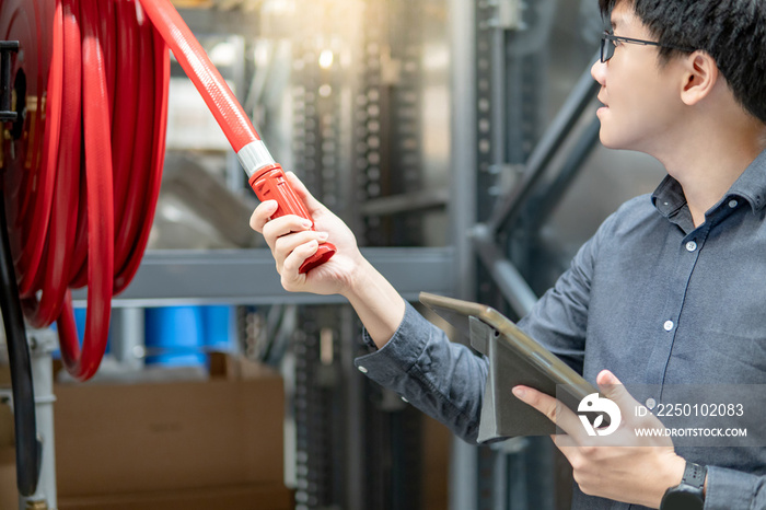 Young Asian male technician checking red fire hose reel by using digital tablet. Building service an