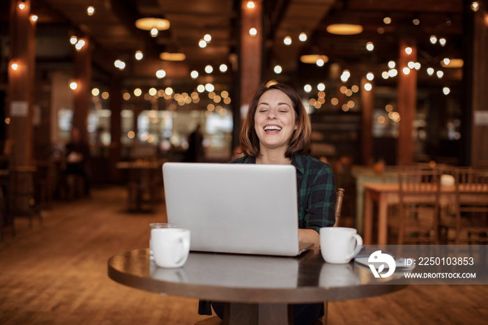 Happy businesswoman video conferencing over laptop computer while sitting against illuminated lights