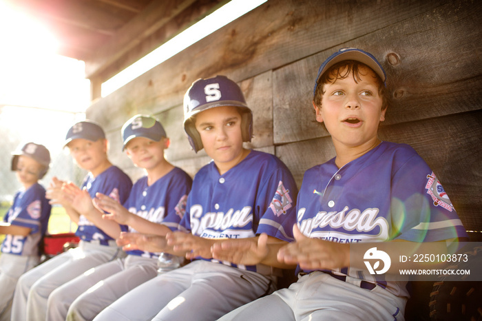 Little league team (8-9) cheering together in dugout