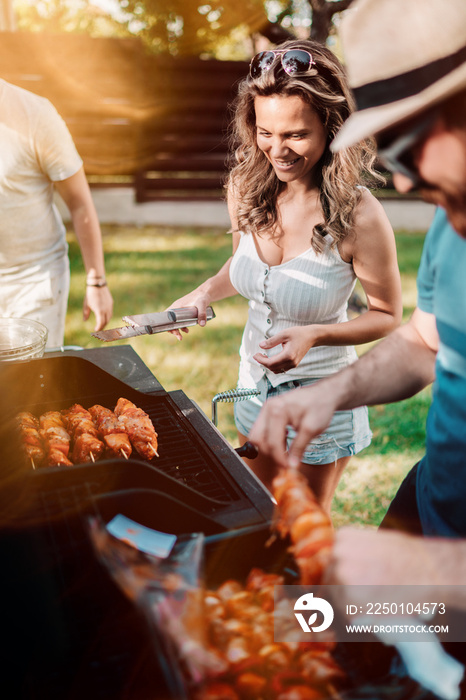 Happy woman cooking on barbecue grill with friends