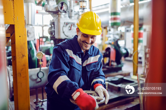 Smiling hardworking energy plant worker in working suit screwing valve.