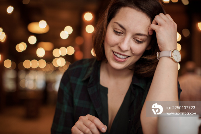 Close-up of smiling businesswoman looking down while sitting against illuminated lights in coffee sh