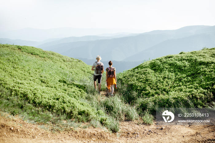 Beautiful couple walking with backpacks on the green meadow, while traveling high in the mountains d