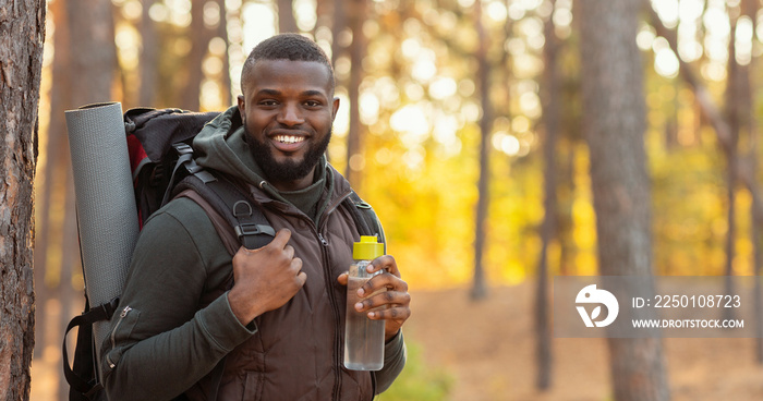 Happy guy with backpack smiling over forest background