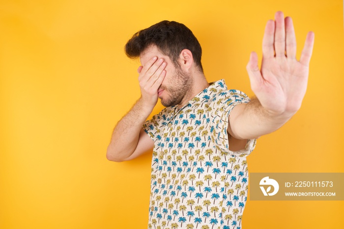 People, body language. Young man covers eyes with palm and doing stop gesture, tries to hide from ev