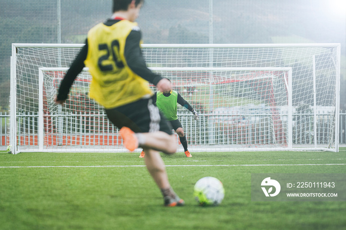 训练中注意力不集中的男足球运动员将球踢向守门员的后视图