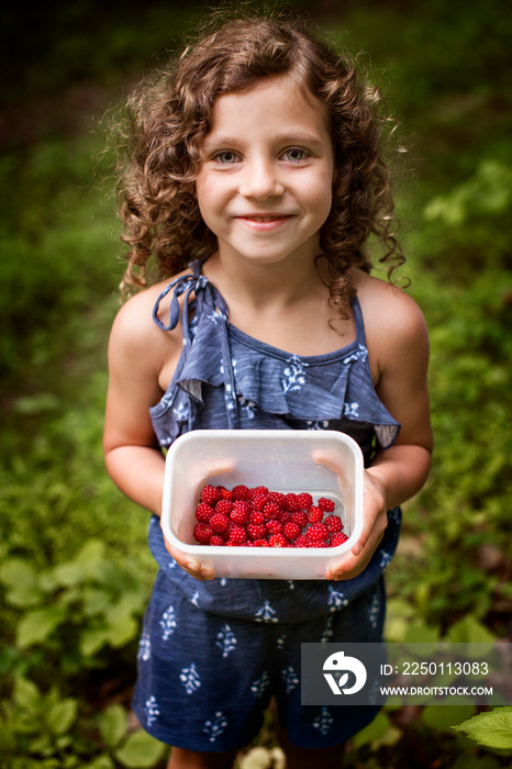 Girl (4-5) with curly hair holding box with raspberries in forest