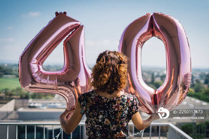 Attractive curly brunette celebrating her 40th birthday with big balloons