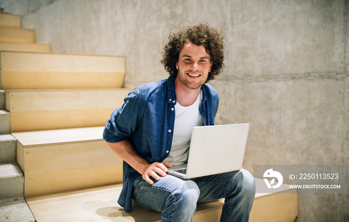 Cheerful male with curly hair using laptop for chatting online with friends, connected to free wirel